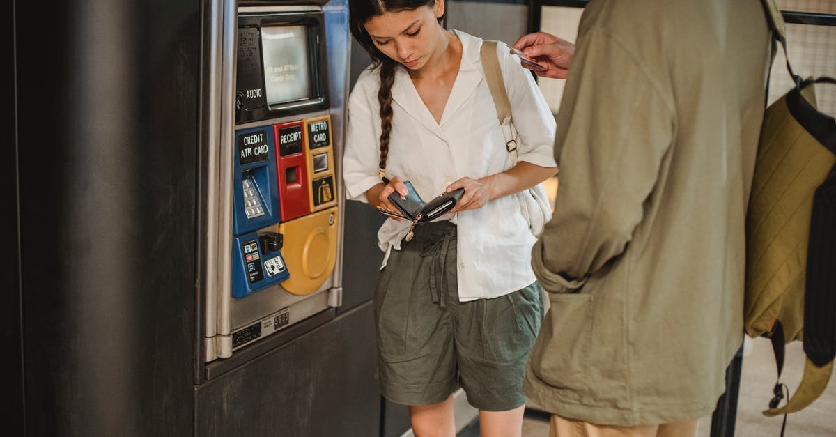 How is TfL underground 'capping' calculated if I pay for multiple people's tickets? - Calm young couple wearing casual clothes standing together near ticket vending machine with wallet in hands in underground