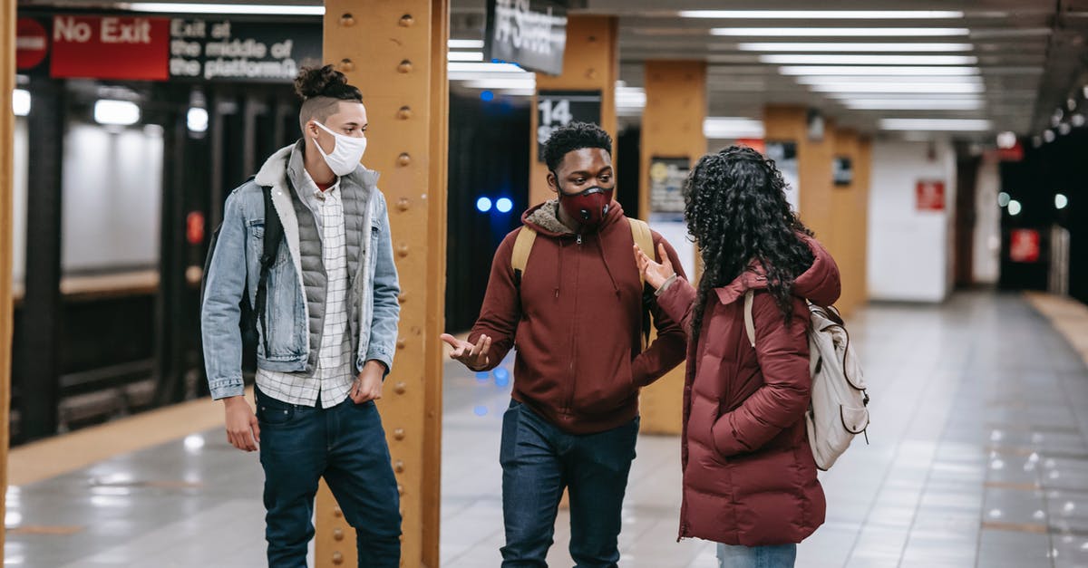 How is Venice during COVID times? - Multiracial group of friends with backpacks wearing protective masks looking at each other while standing on subway station during meeting