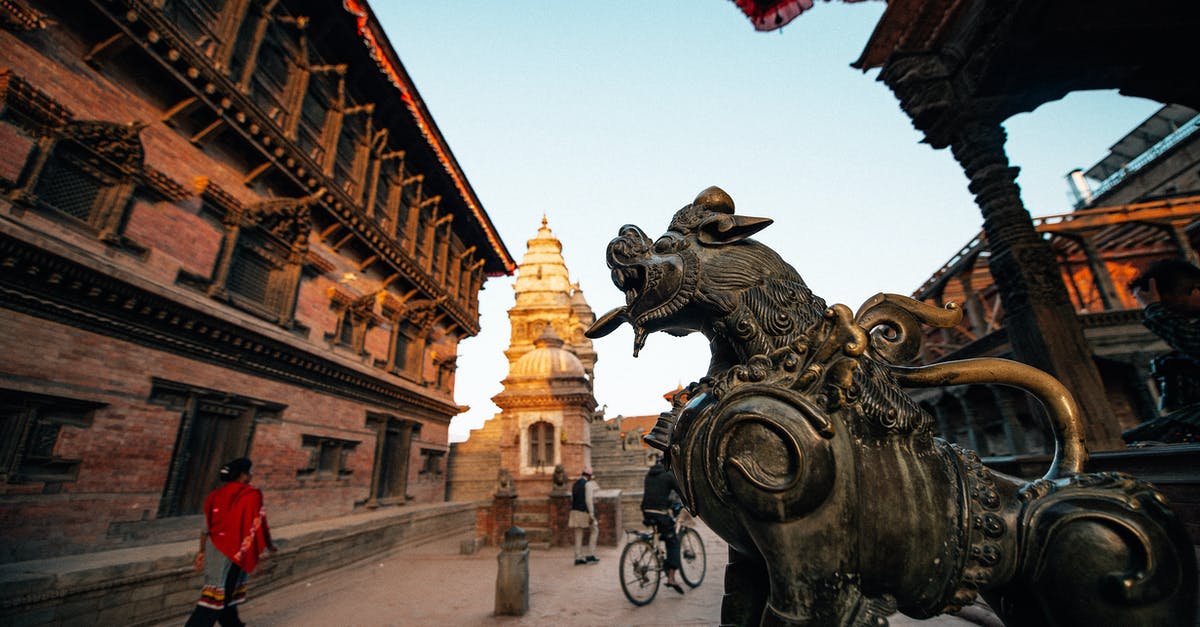 How long can I stay in Nepal on a tourist visa? - From below of aged ornamental statue of animal in front of stone church facade with cupola and unrecognizable tourists walking on pavement under serene sky in evening