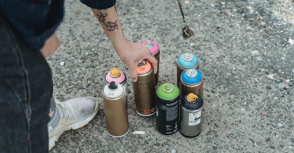How many bottles of perfume can I bring in to India when flying back from Dubai? - Crop faceless tattooed artist taking paint bottle from heap of multicolored spray cans placed on ground on street of city
