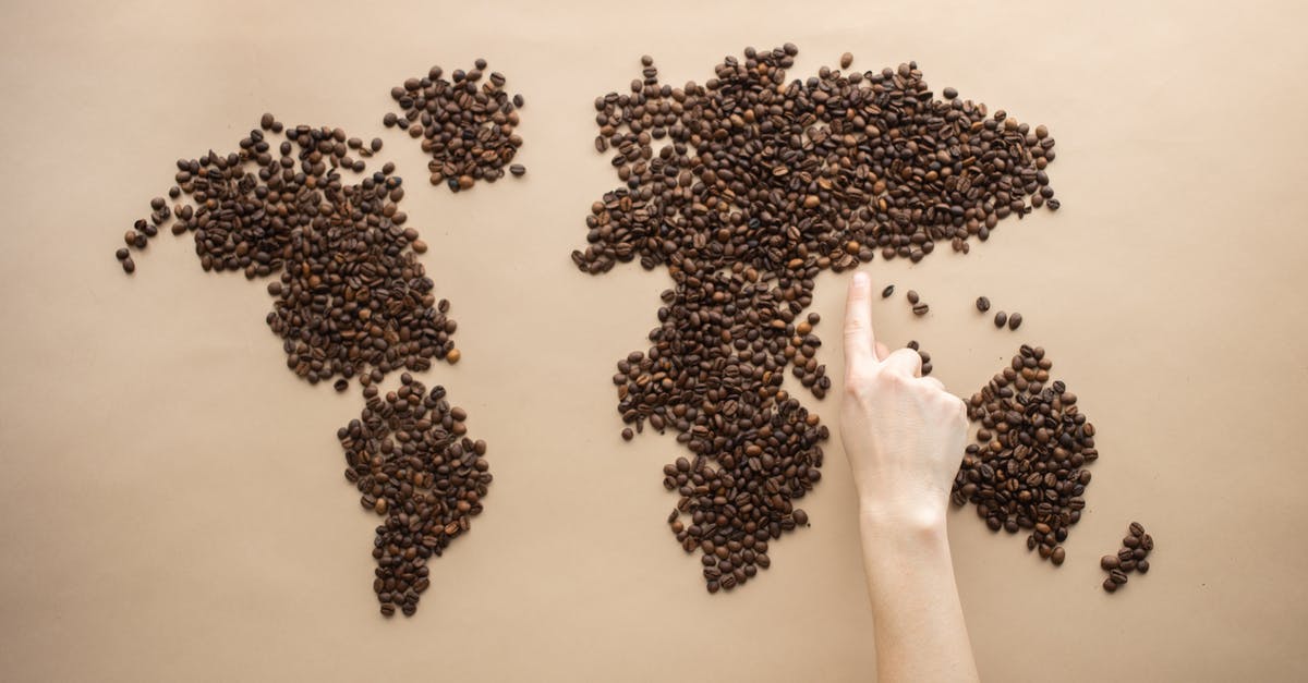 How many laptops are allowed in hand baggage in European flight? - Top view of crop person pointing finger at world map made of coffee beans on brown background