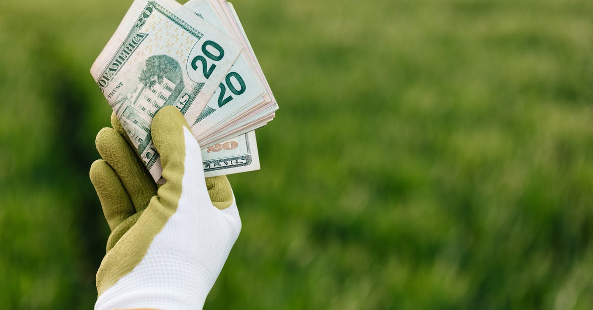 How many tents per campsite in US national parks? - Crop anonymous gardener in gloves showing American paper money with number twenty and photo of building on blurred background with green field in daylight