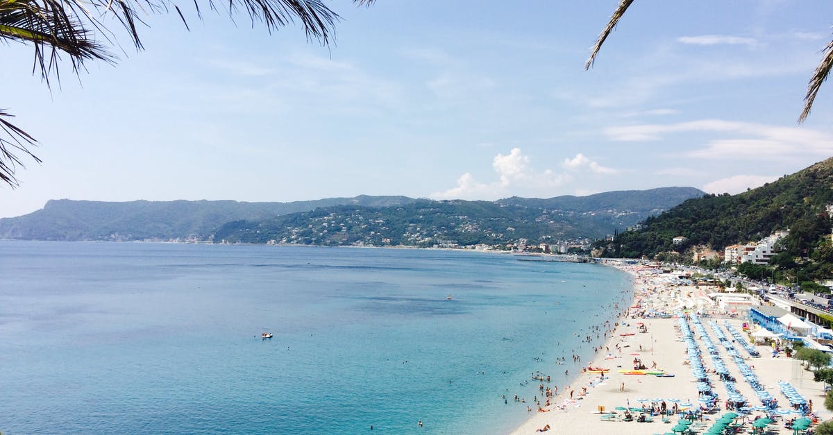 How many years can I get on a Canadian tourist visa? - From above of anonymous travelers on sandy shore with many sun umbrellas near blue sea behind ridge under cloudy sky in summer