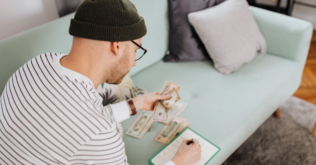 How much cash do I need when entering Germany? - Man Writing on a Notebook While Holding His Money 