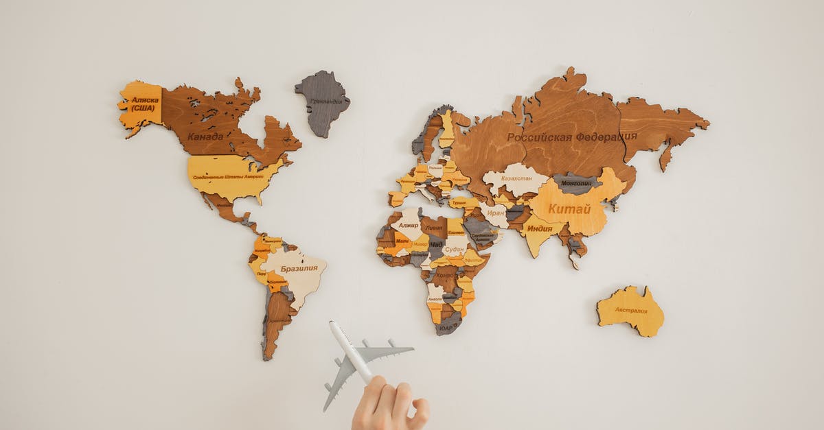 How much does it add to a North America / Australia journey to go "the wrong way"? - Crop unrecognizable person with toy aircraft near multicolored decorative world map with continents attached on white background in light studio