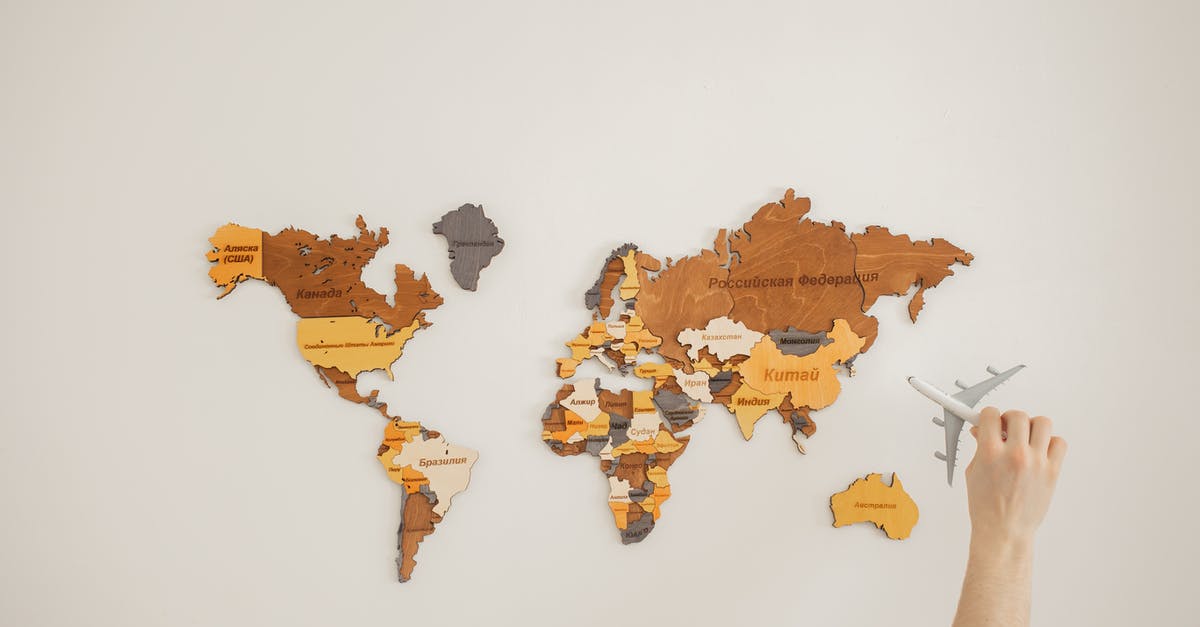 How much does it add to a North America / Australia journey to go "the wrong way"? - Crop anonymous traveler with toy aircraft over decorative wooden world map with country names on white background in light room