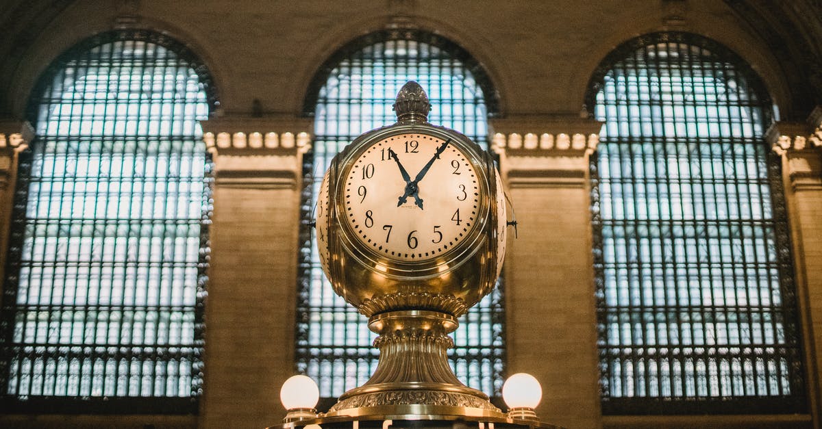 How much extra time should I reserve to enter the US from Canada with the Windsor-Detroit Tunnel Bus as a European VWP citizen? - From below of aged retro golden clock placed atop information booth of historic Grand Central Terminal with arched windows