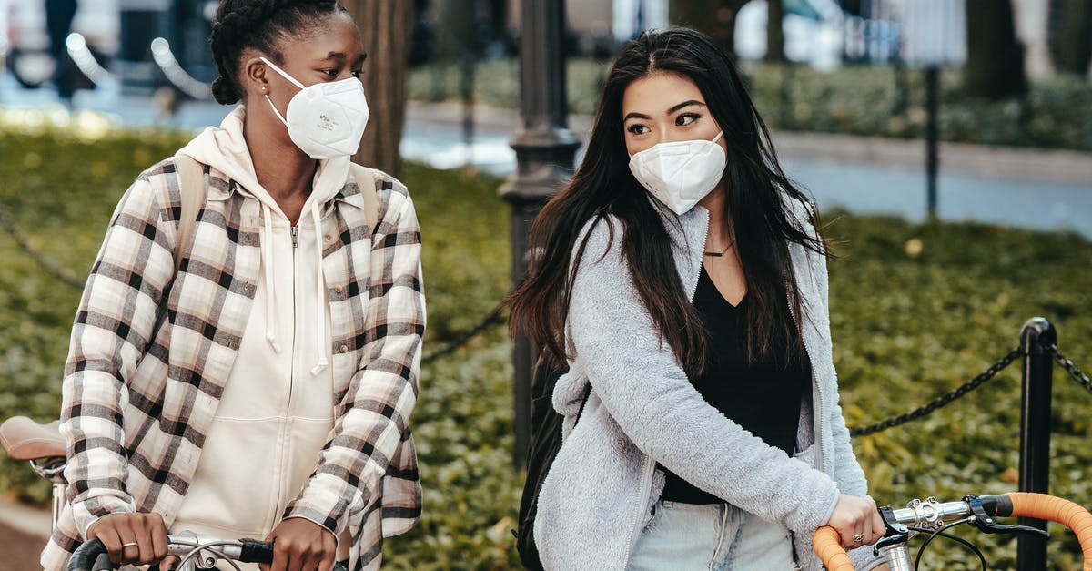 How much is a safe minimum layover time? - Multiethnic girlfriends in masks talking to each other while strolling with bicycles in park during COVID pandemic