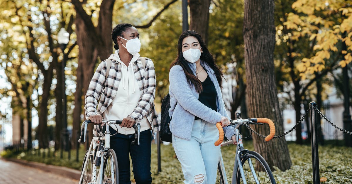 How much is a safe minimum layover time? - Diverse girlfriends with bicycles walking on pavement in park