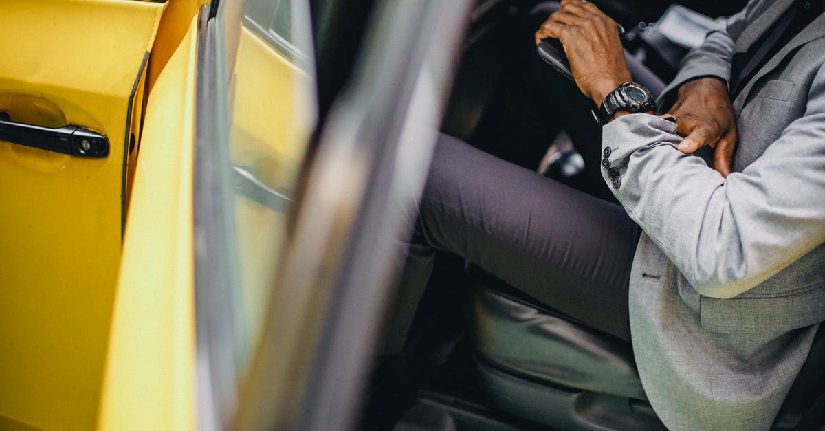 How much time is needed for check-in at Zurich? - Side view of crop anonymous African American male in elegant suit checking wristwatch in car