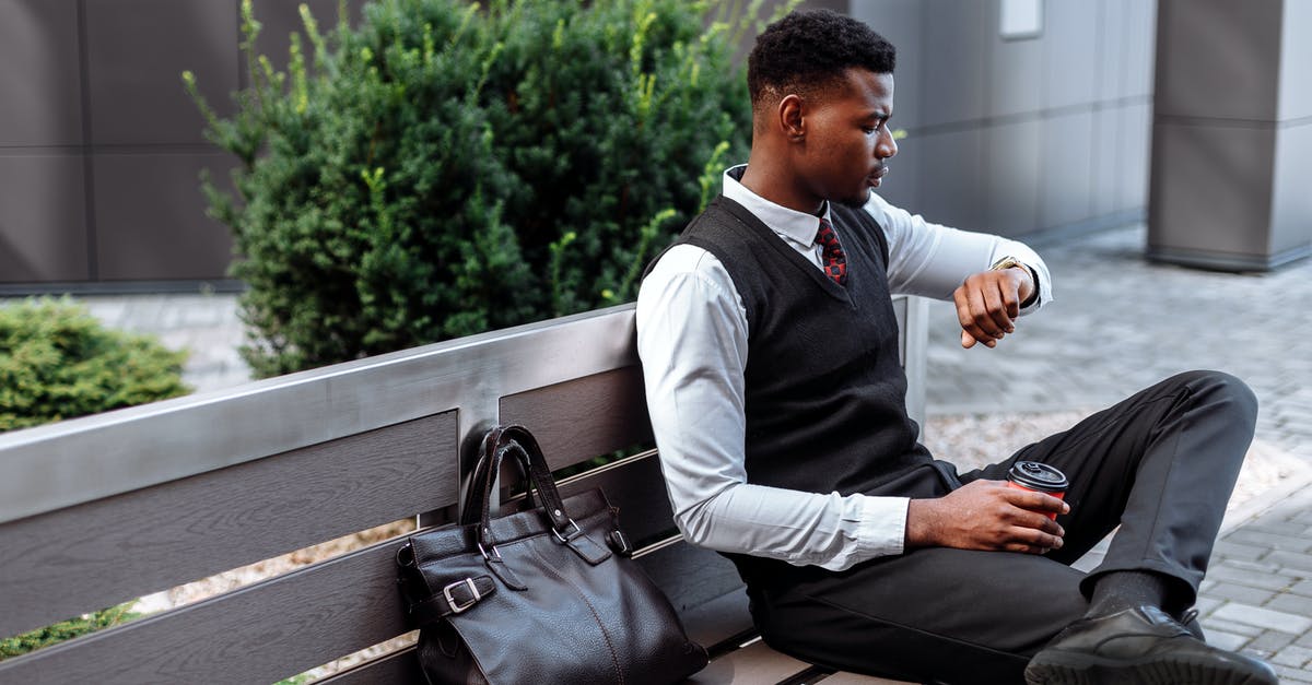 How much time is needed for check-in at Zurich? - Man in Black Vest Checking the Time on His Wristwatch while Sitting on a Wooden Bench