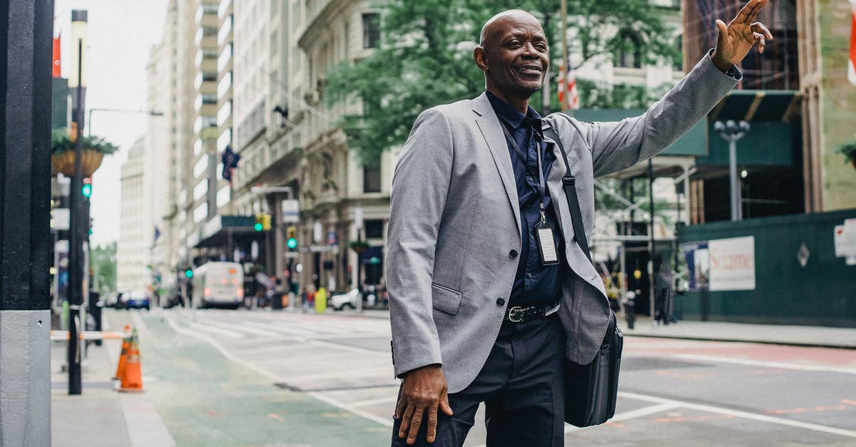 How reliable is public transport in Colombia? - Cheerful successful African American entrepreneur waiting for taxi on local street of modern city