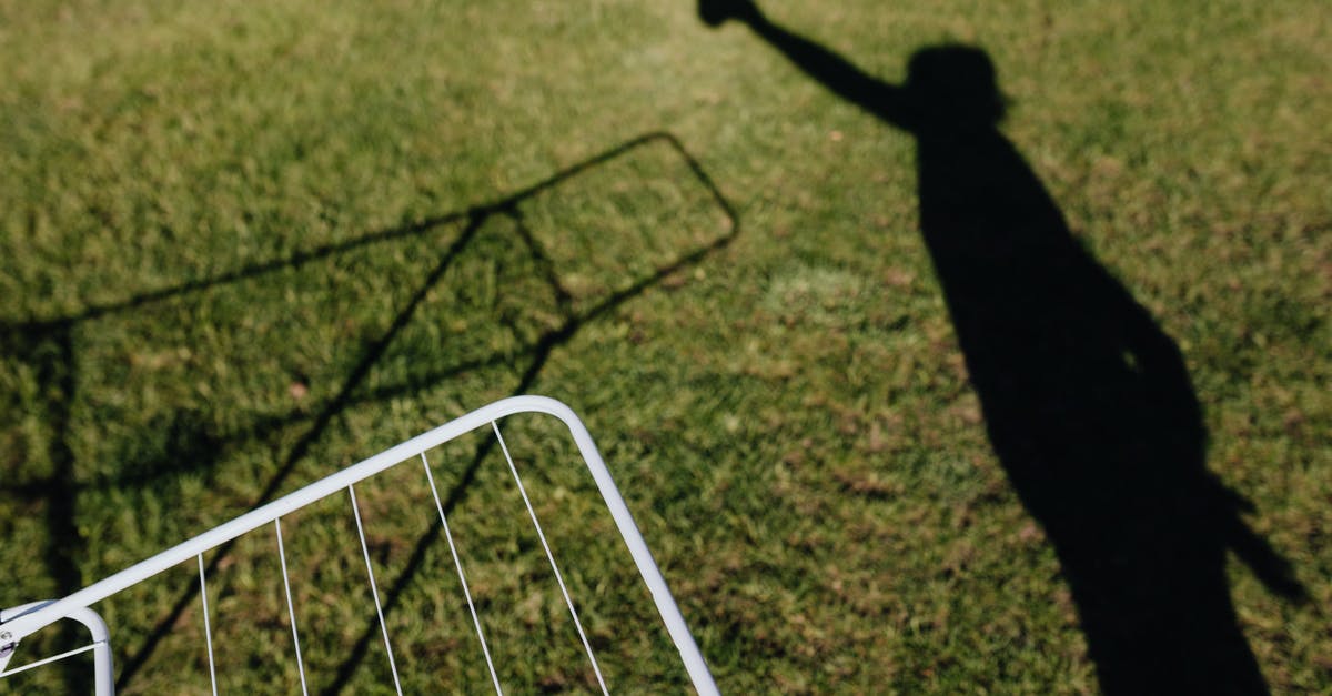 How should I wash clothes in Iceland? - From above of metal dryer fragment with no clothes standing on grass outdoors and shadow of person imitating clothes hanging on drying rack on sunny summer day