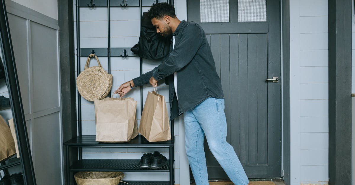 How should one prepare for a business trip to Manila? - Man in Black Long Sleeve Shirt and Blue Denim Jeans Standing Beside Black Wooden Door