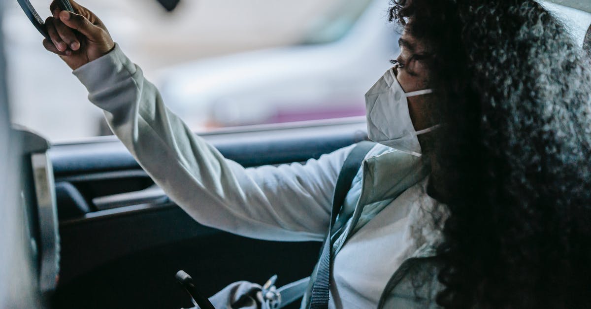 How to access the internet during a road trip in the USA? - Side view of anonymous young African American female passenger in casual clothes and protective mask holding handle and looking away while sitting on backseat of taxi with smartphone in hand