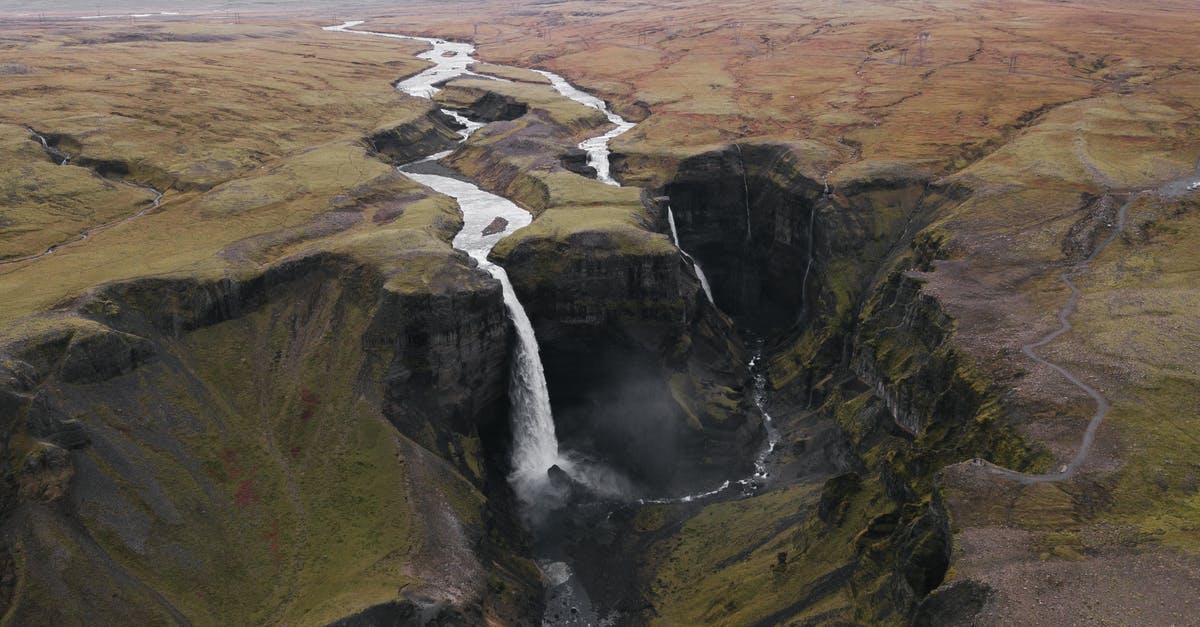 How to assess rough water severity? - Breathtaking distant scenery of rocky relief covered with mosses and lichens with river and waterfall flowing into narrow ravine under gray cloudy sky