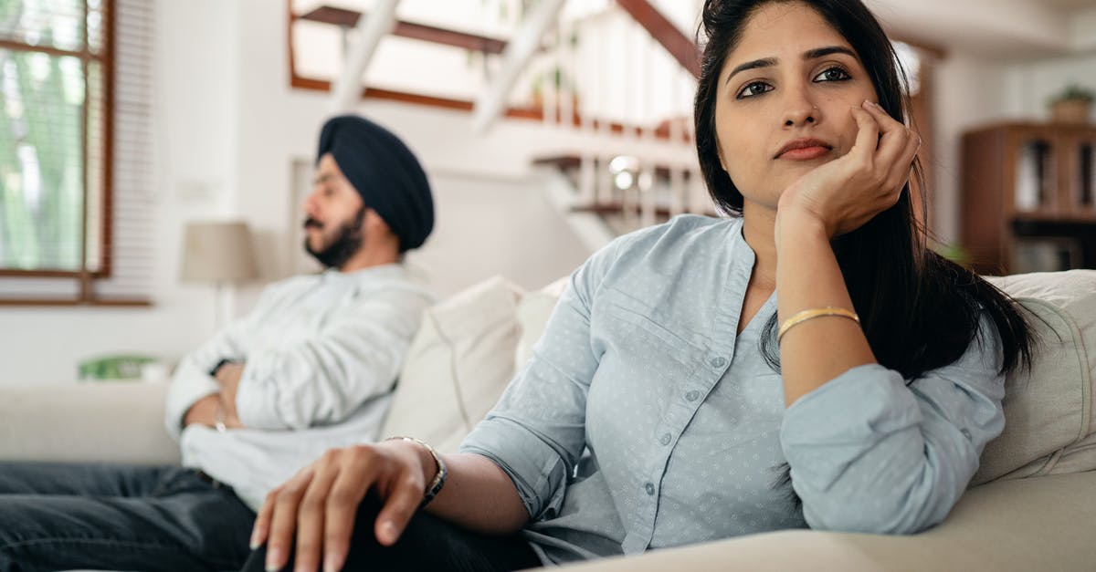 How to avoid claustrophobia on a plane? - Sad young Indian woman avoiding talking to husband while sitting on sofa