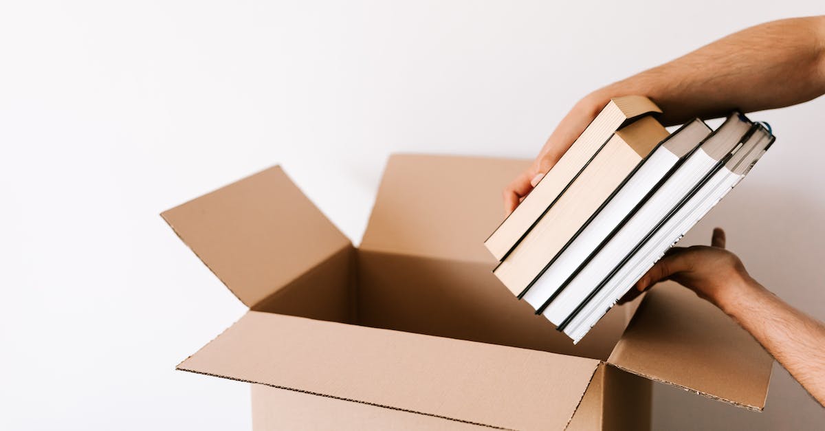 How to book courier flights (discounted fare in exchange for delivering a package upon arrival)? - Crop unrecognizable male packing staked books into carton box while standing against white wall during relocation