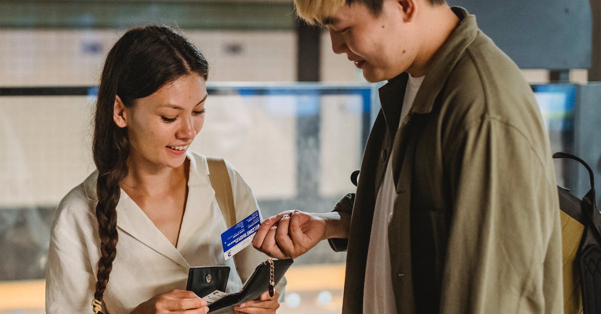 How to buy a flight ticket for someone else in Condor? - Content Asian couple in casual clothes opening wallet and buying tickets for public subway standing in underground passage