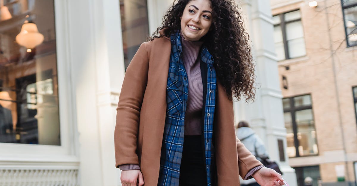 How to carry phones as presents to the USA from Europe? - Low angle of positive ethnic female in coat above casual wear standing with bright gift bags on sidewalk and looking away