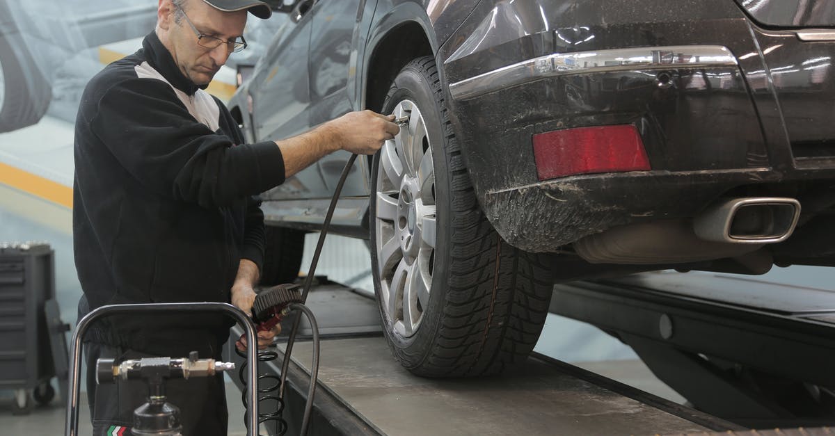 How to check safety of car rental offer in Spain? - Serious car mechanic pumping up car wheel in modern service garage