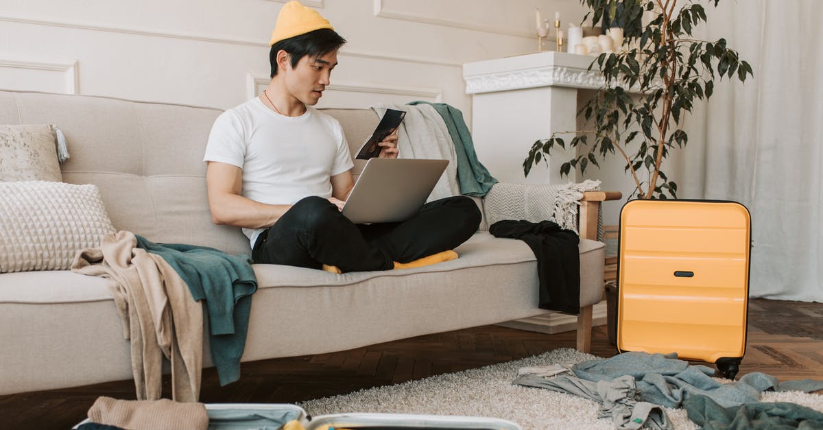 How to deter theft of checked baggage at baggage carousels? - Man in White Crew Neck T-shirt and Black Pants Sitting on Gray Couch Using Black