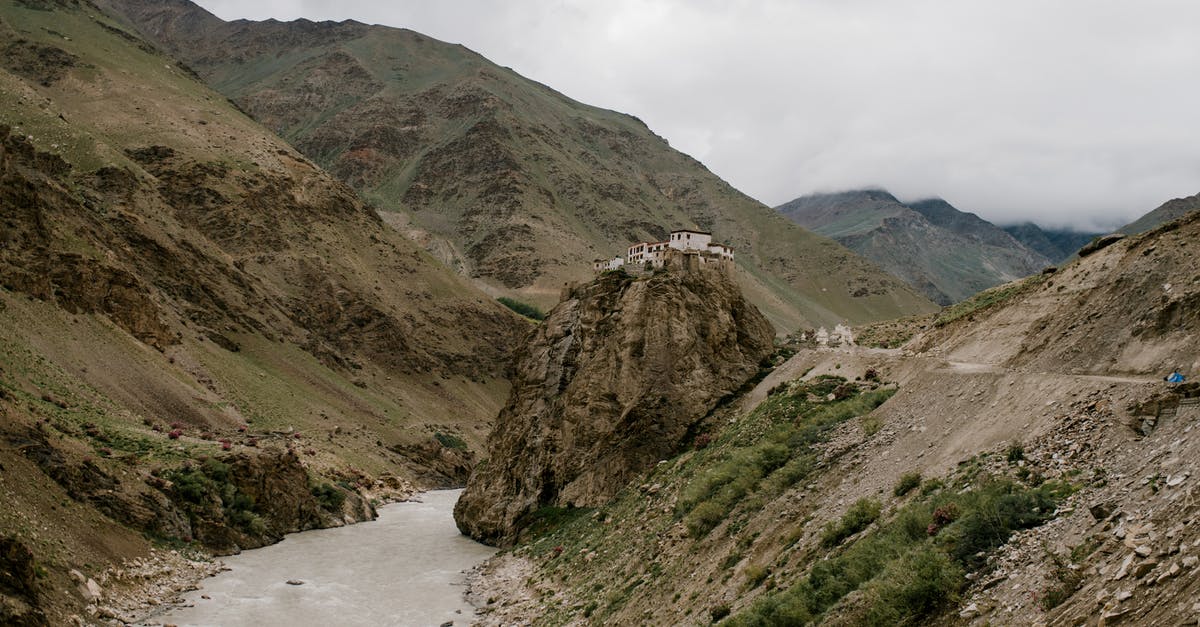 How to dress suitably for Jungfrau mountain sightseeing trip? - Picturesque scenery of wild river flowing among rough rocky mountains near old Buddhist Bardan Gompa monastery against foggy sky