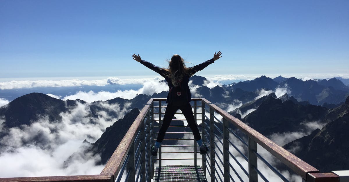 How to enjoy traveling with more people - Person Standing on Hand Rails With Arms Wide Open Facing the Mountains and Clouds