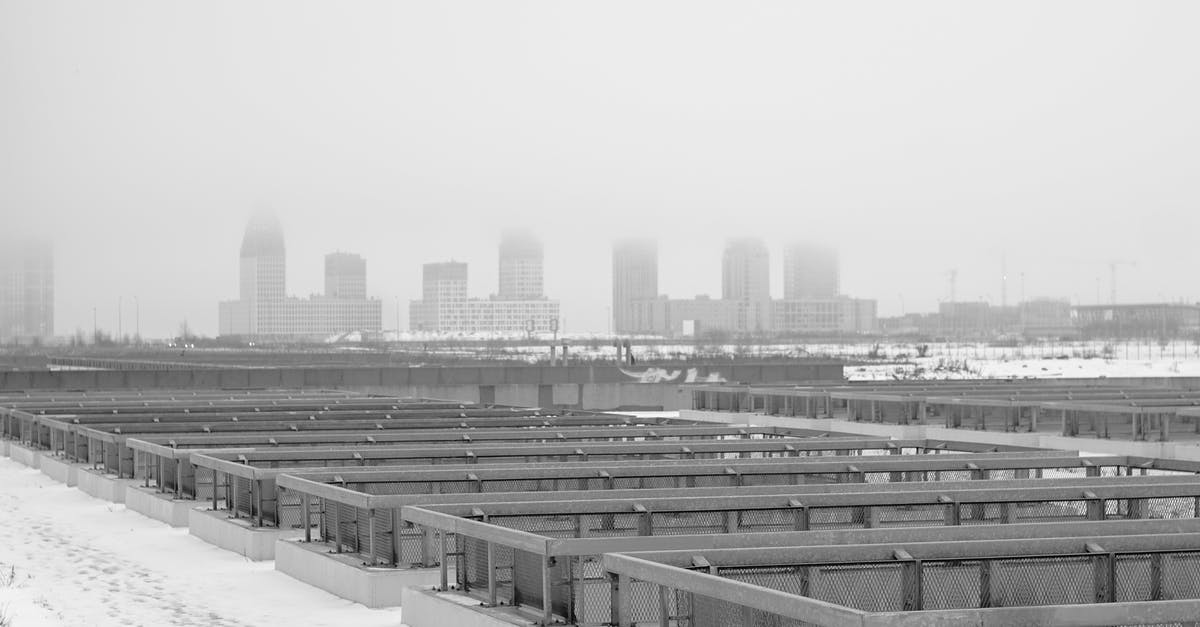 How to find cities with similar weather conditions - Black and white of industrial constructions in rows on snowy land against multistage buildings in town