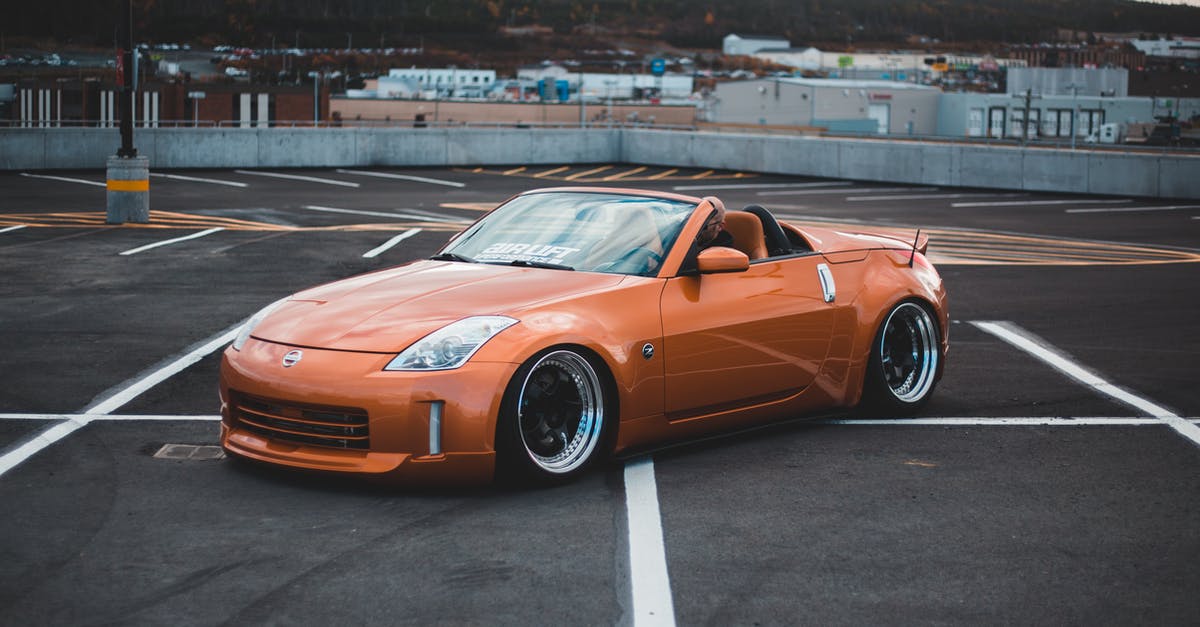 How to find mountain parking in Switzerland? - From above side view of modern style automobile with convertible top on asphalt pavement with marking lines in city parking lot behind cement fence and mountain with trees