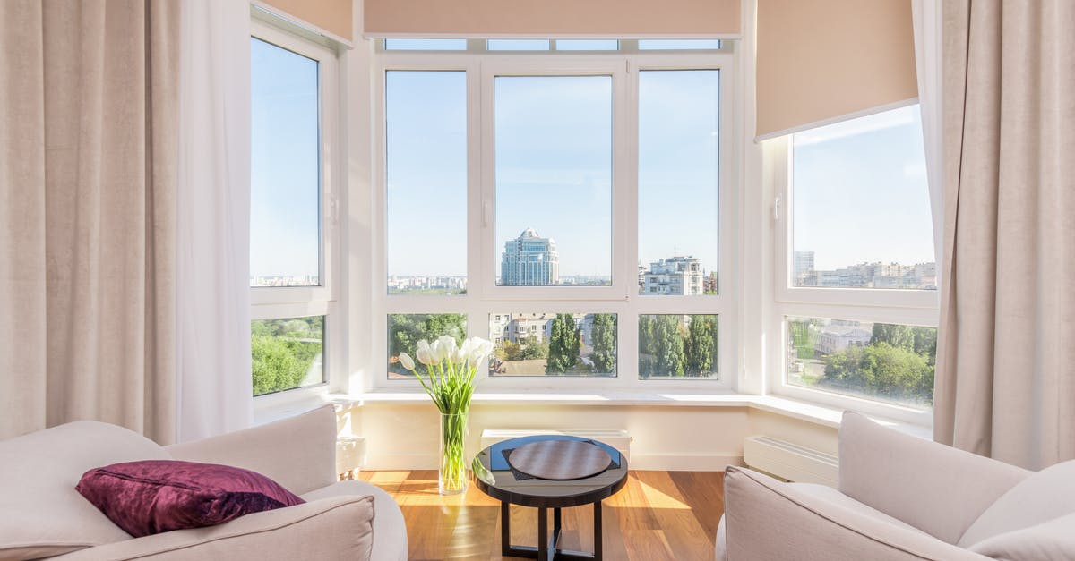 How to find neighboring apartments/self-catering accommodation? - Interior of modern penthouse with comfortable white armchairs and round side table placed near windows overlooking city in sunny day