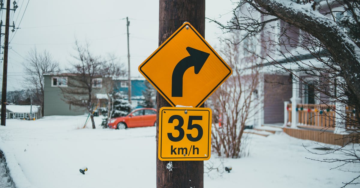 How to find out the speed limit in the US? - Control road signs with arrow showing turn under speed limit on post against buildings with snow in wintertime