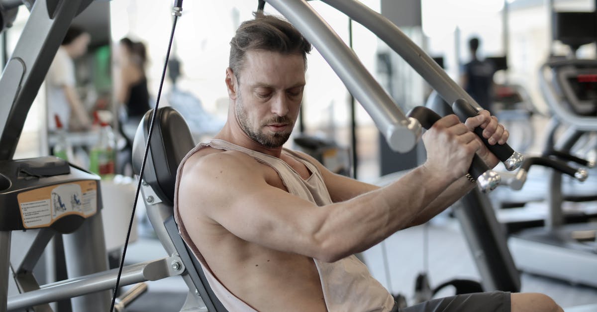 How to find out your body weight while travelling? - Side view of confident muscular man doing exercises on shoulder press machine while training in modern sports center