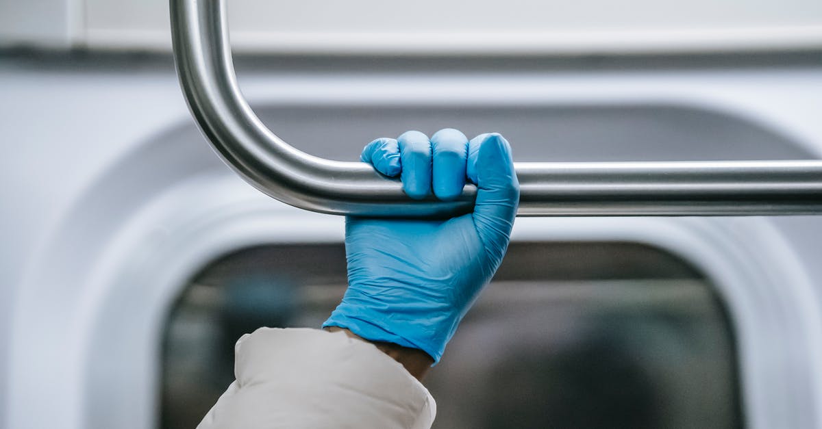 How to find safe places to travel during the pandemic? - Crop anonymous African American person in warm clothes and protective glove grabbing overhead handle while riding metro train during coronavirus outbreak