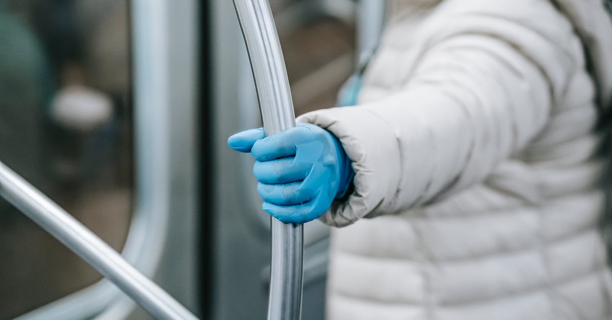 How to find safe places to travel during the pandemic? - Side view crop person in outerwear and latex gloves holding handle and riding underground train during coronavirus epidemic