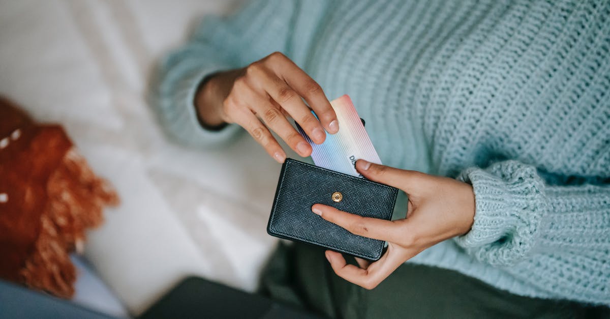 How to get a Smart Card for the Cairo metro? - From above crop anonymous female in casual sweater taking credit card from wallet and lying on bed with laptop before making online purchase