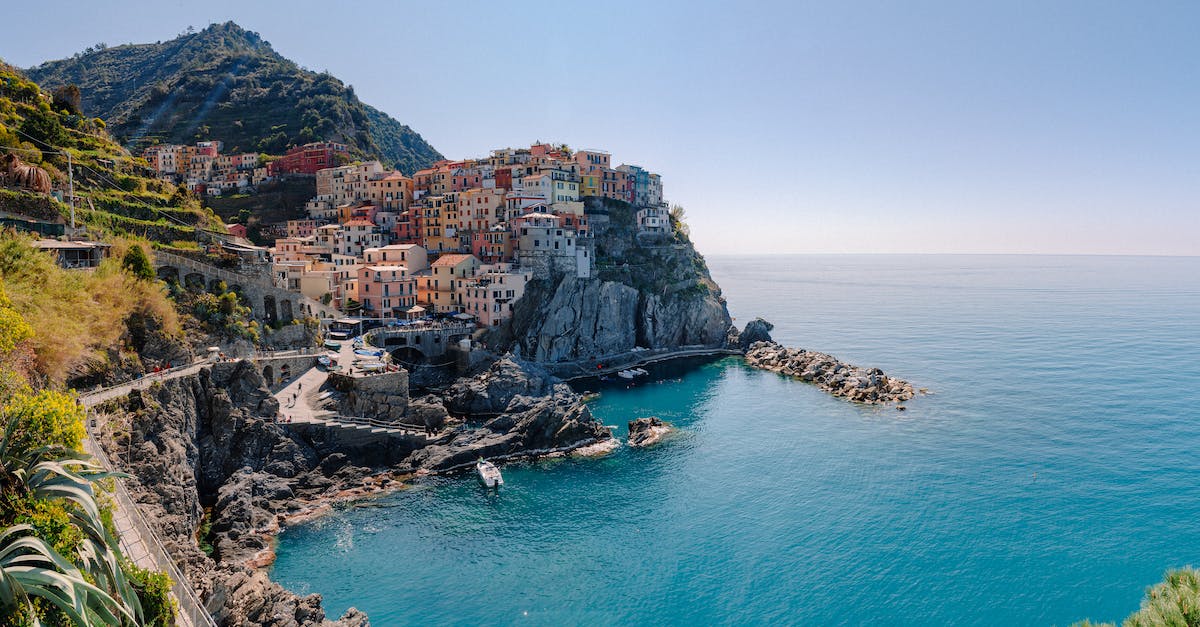 How to get from Genoa to Cinque Terre? - Breathtaking scenery of historic colorful buildings of famous coastal Manarola town located on stony hill in front of turquoise sea on sunny day