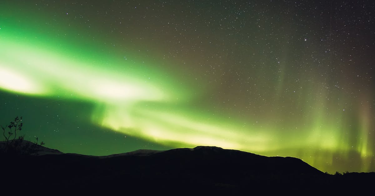 How to get from North Wales to Cambridge? - Low angle scenery view of bright green northern lights illuminating mountain silhouette and starry sky in evening