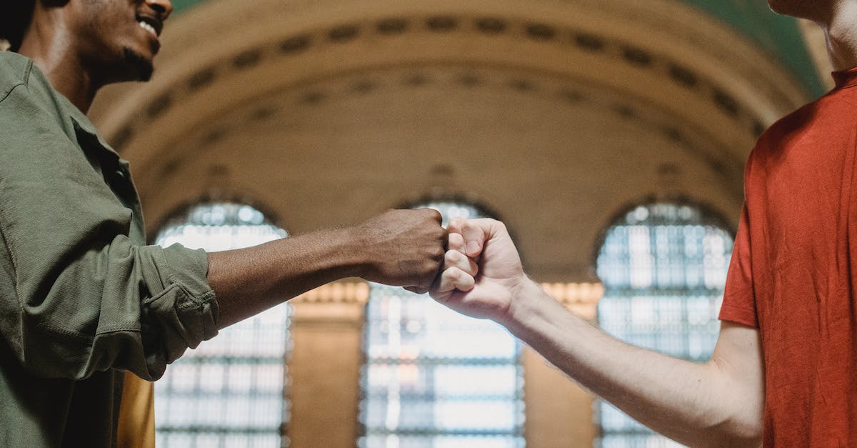 How to get to Old Trafford from Piccadilly station? - From below of crop multiethnic friends in casual clothes giving fist bump against arched wall and windows in aged hallway of Grand Central Terminal placed in New York City