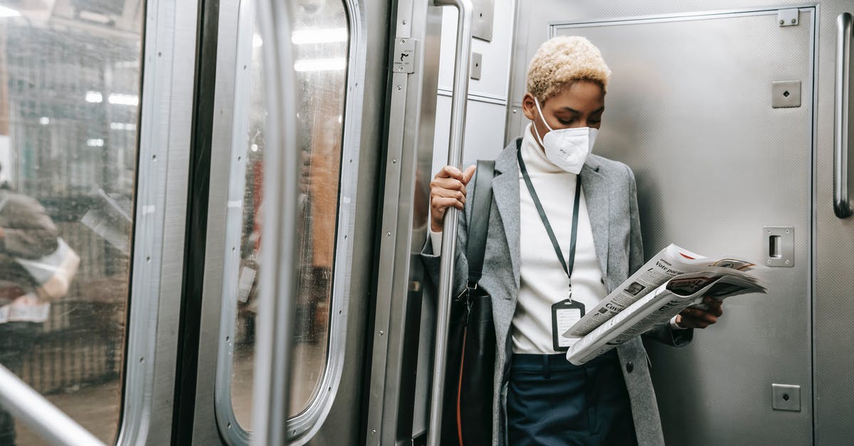 How to get updated about current incidents and safety concerns? - Concentrated young African American female in formal outfit and protective mask reading fresh newspaper while standing in metro train corner