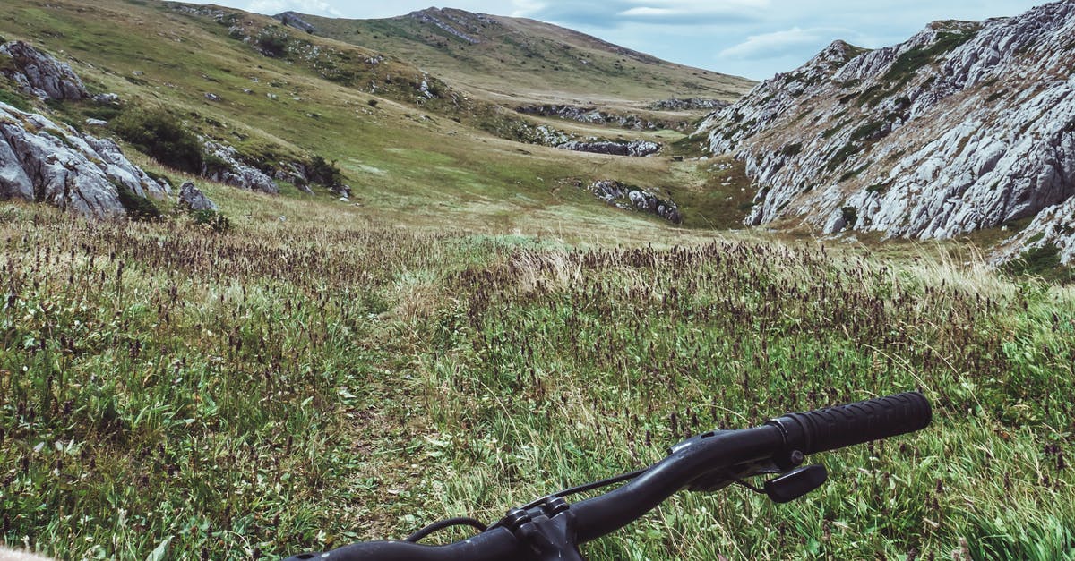 How to handle payments while travelling to Indonesia? - Person Riding Bicycle Overlooking Green Grass Field and Hill