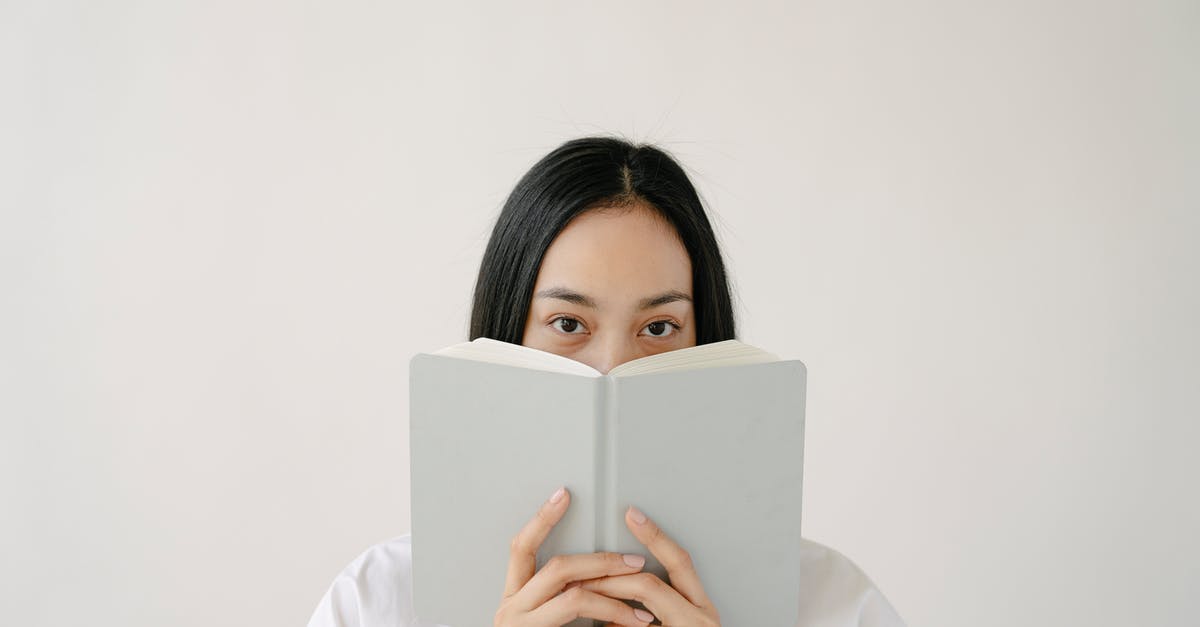 How to hide your bodily odors after a long flight? - Young ethnic female student with long dark hair covering face with notebook while preparing for exams against white background