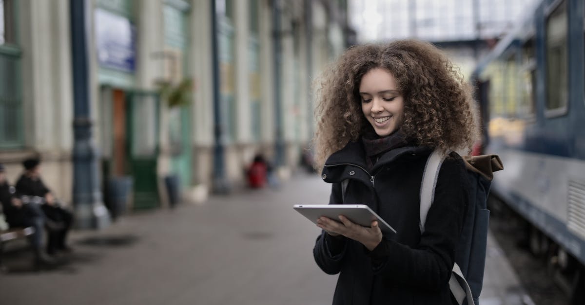 How to keep electronics warm in cold countries? - Cheerful young lady browsing tablet while waiting for train on platform