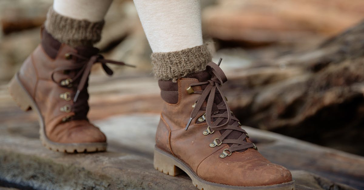 How to keep electronics warm in cold countries? - From above female feet in light tights and casual warm autumn boots standing on wooden log against shabby wooden planks