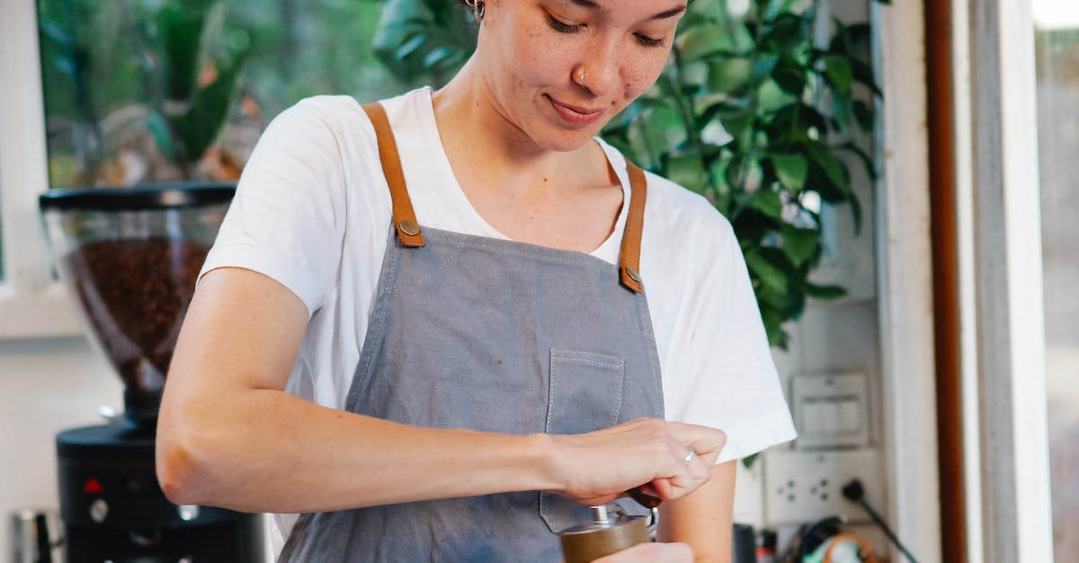 How to make the best use of signs while hitchiking? - Crop happy female in apron smiling and using grinder for preparing aromatic coffee in kitchen