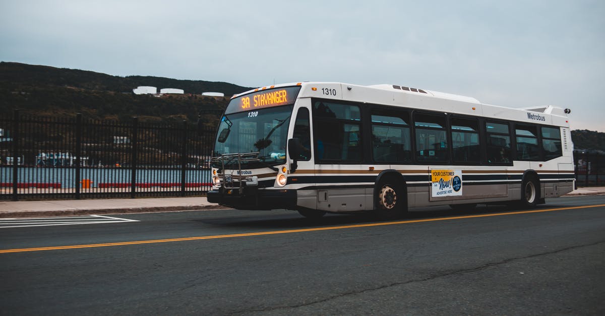 How to manage a longer transit location in a cheaper way - Big gray bus driving on asphalt highway along metal fence near water against cloudless sky with mountains in distance outside