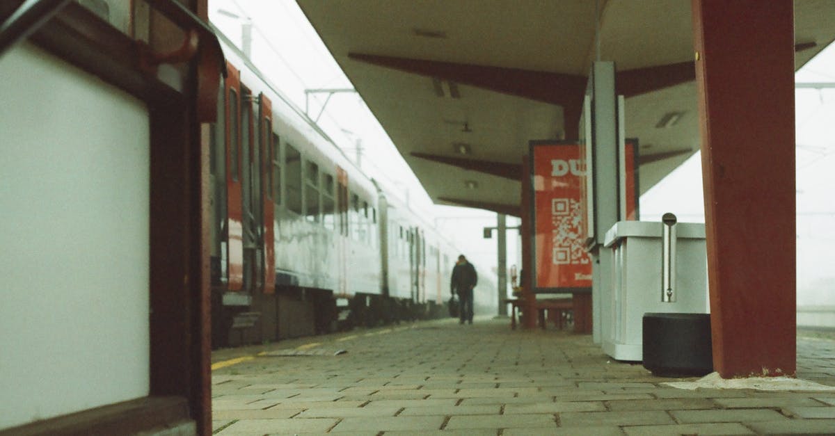 How to manage a longer transit location in a cheaper way - Unrecognizable male traveler walking on platform of railway station near modern train against cloudy sky