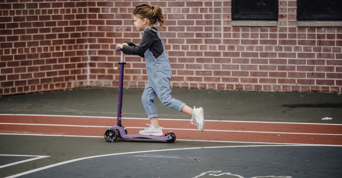 How to move children in a Las Vegas casino? - Side view of excited preschool girl in casual outfit riding scooter on asphalt sports ground