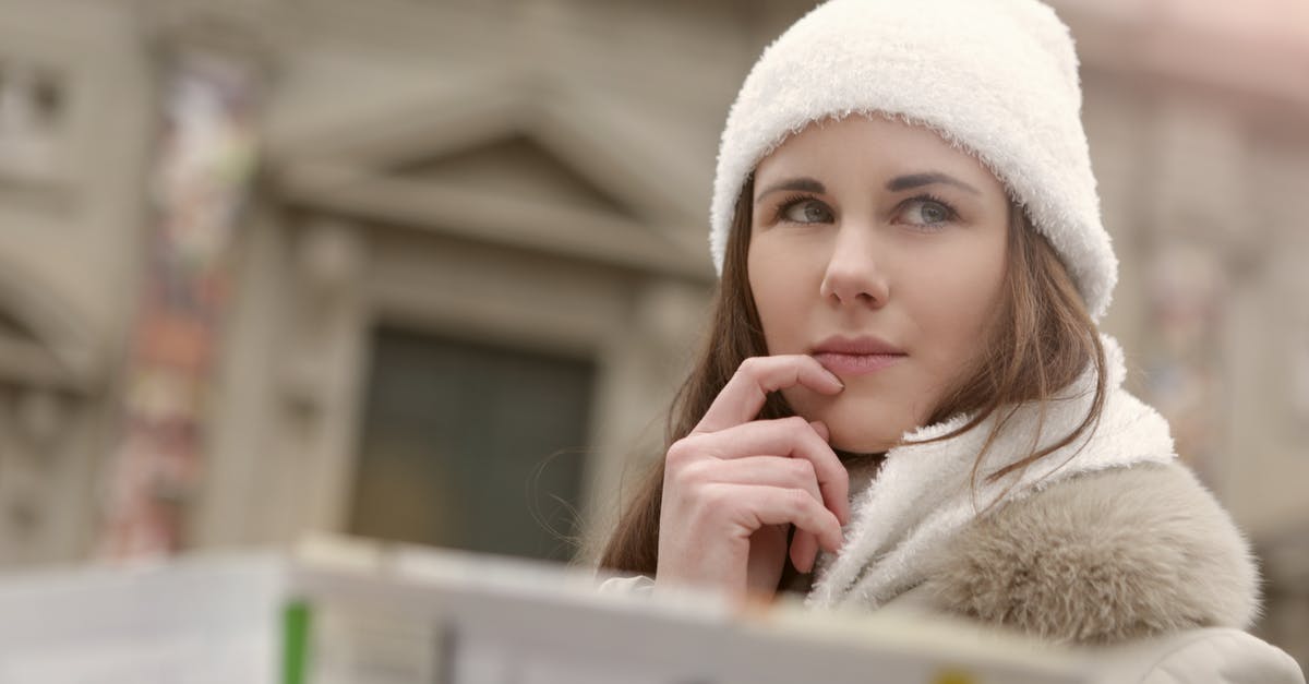 How to plan a road trip with stops on specific dates - Concentrated female in warm hat and coat looking for right way while standing with map in street