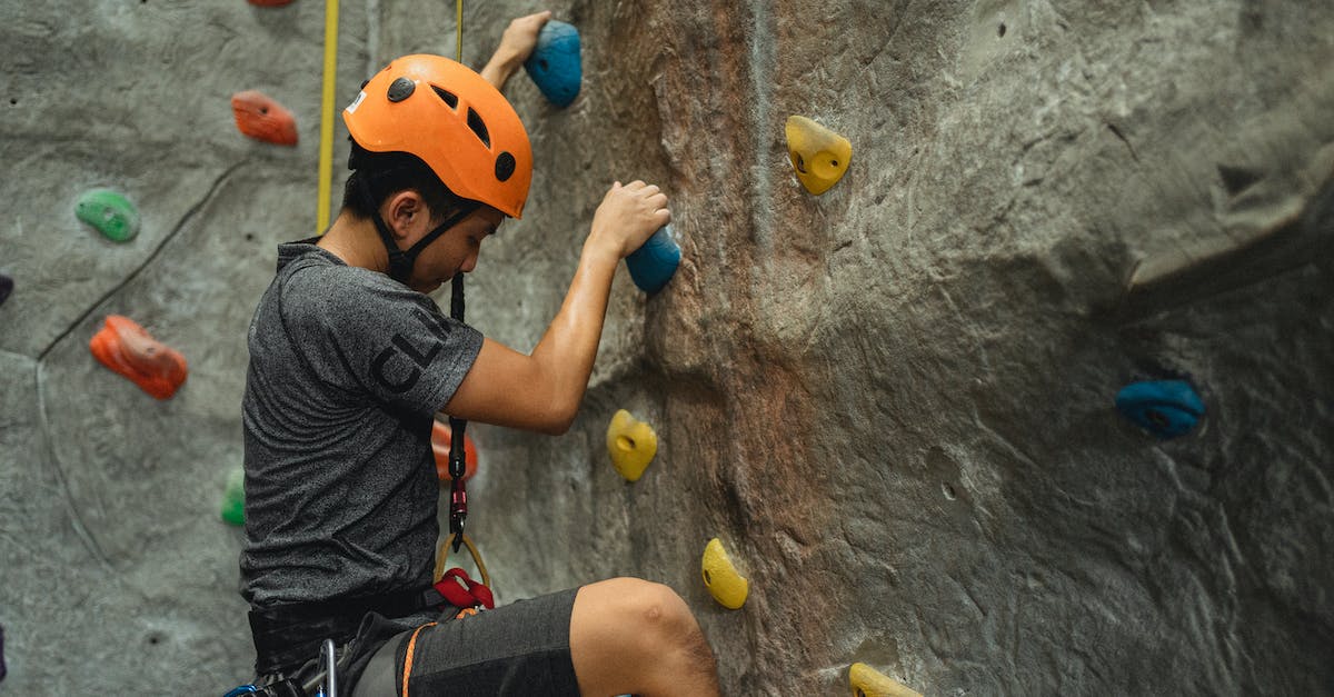 How to protect my gear during a monsoon? - Side view of crop young Asian man in orange helmet and belay ascending on climbing wall during training in bouldering center